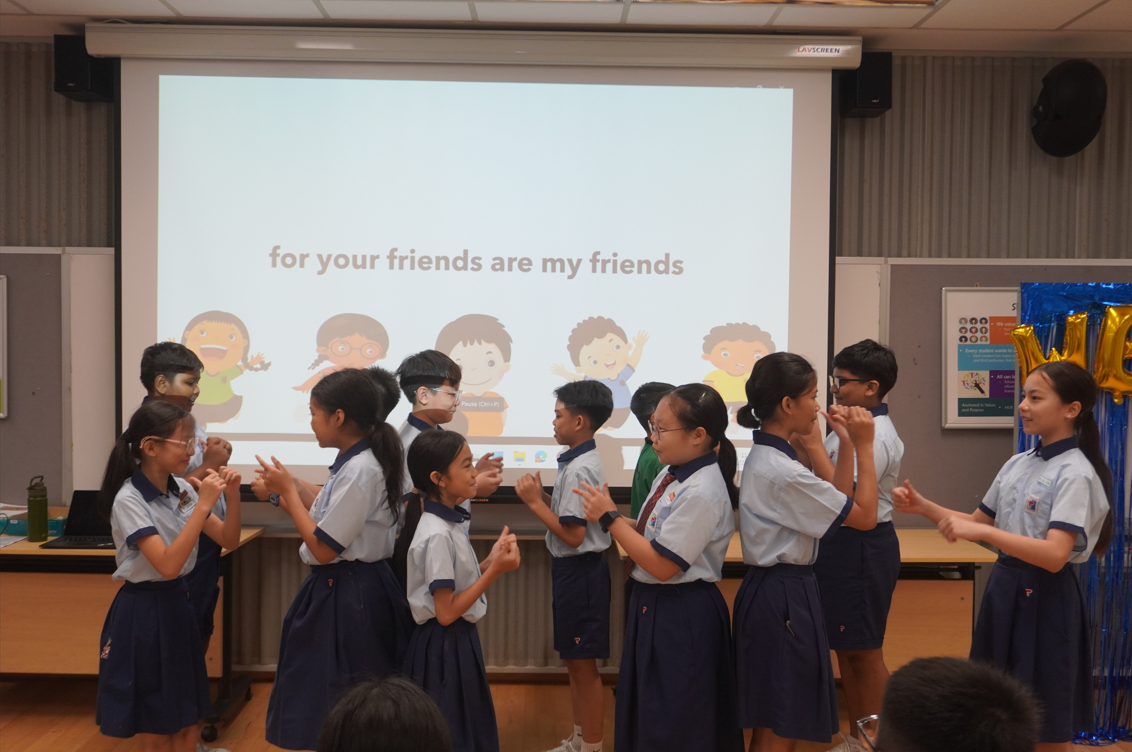 Students standing in two rows facing each other and playing a hand-clapping game in front of a presentation screen.